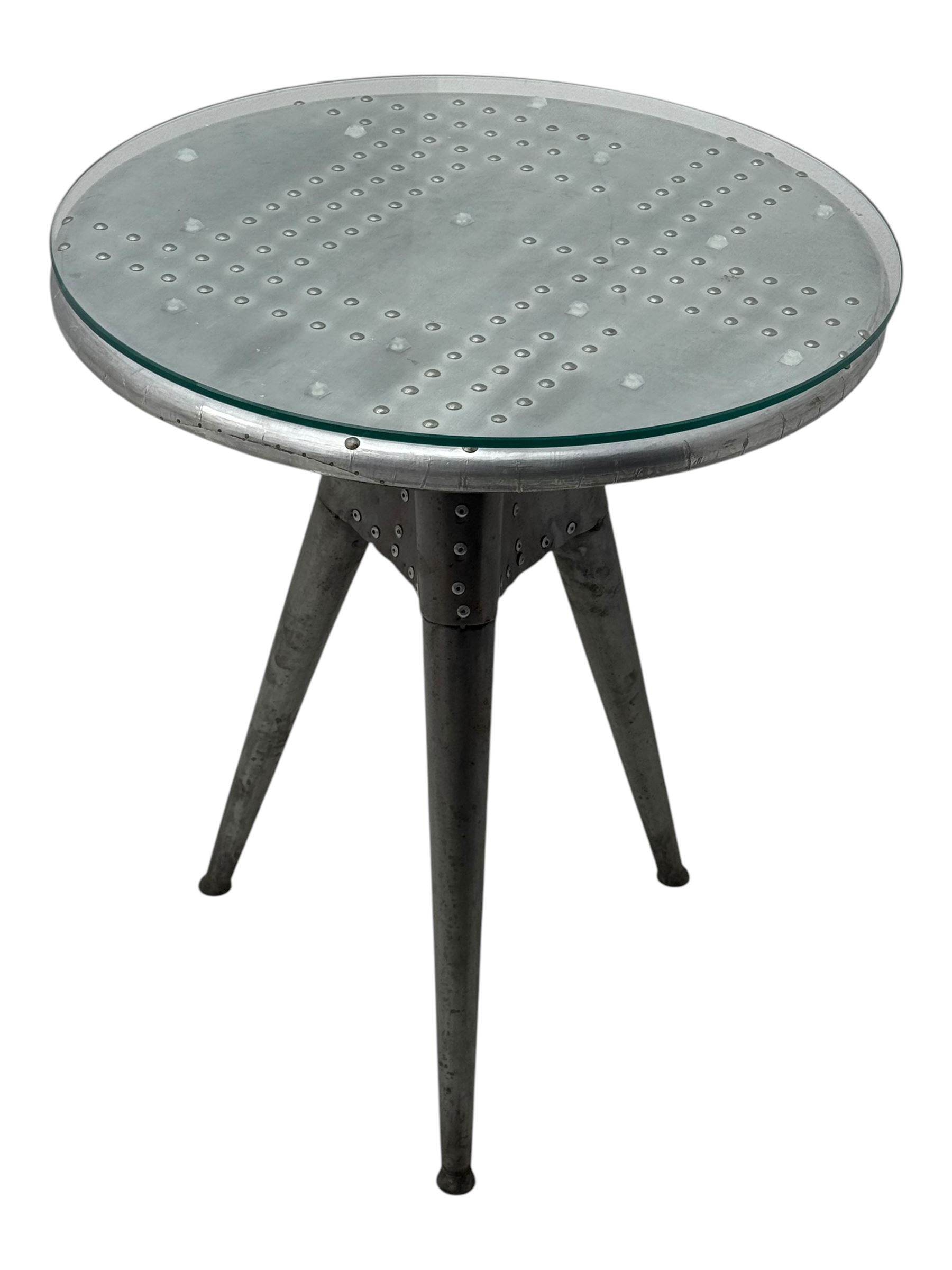 Contemporary industrial design riveted metal table, by repute fashioned from salvaged aeroplane parts, with a circular glass top on a tripod base, accompanied by three adjustable stools upholstered in burgundy