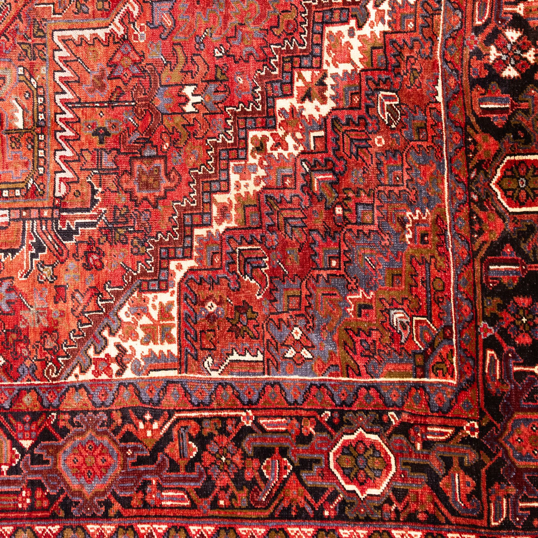 North West Persian Heriz hand-knotted carpet, madder red field, with a large central angular star medallion with stepped outlines on ivory ground, surrounded by geometric floral devices and stylized rosettes, with corresponding corner spandrels, enclosed by a bold geometric main border with multiple guard stripes, with cotton fringe ends 