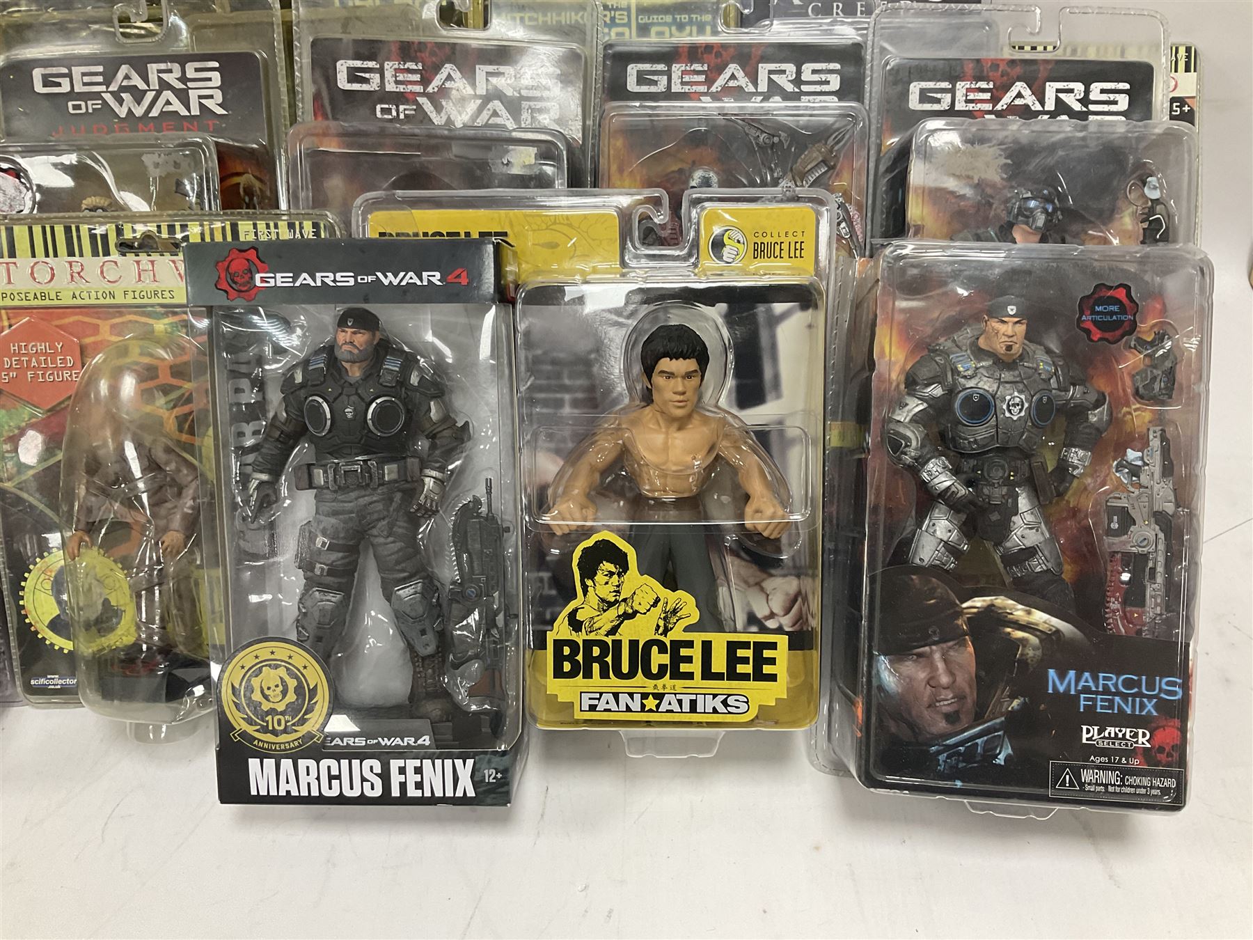 Sixteen carded action figures comprising seven 'Gears of War'; four 'Hitchhikers Guide to the Galaxy'; two 'Torchwood'; 'Planet of the Apes'; 'Bruce Lee'; and 'Assassin's Creed'; all in unopened packs (16)