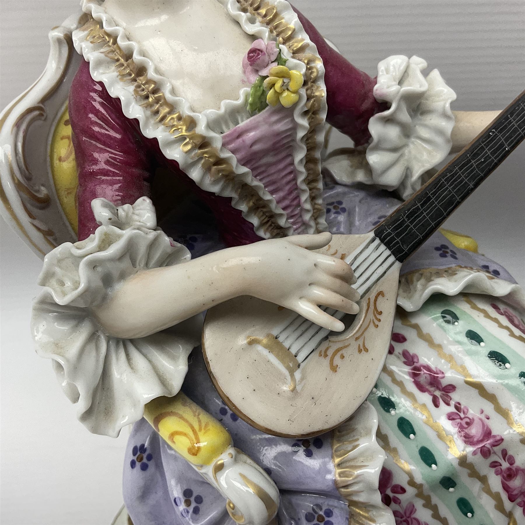 20th century Naples figure group, modelled as a seated female figure playing the lute seated, before a male figure stood holding a sheet of music, each in period dress, upon an oval base with gilt heightened scroll edge, with crowned N mark beneath, H31.5cm L33cm
