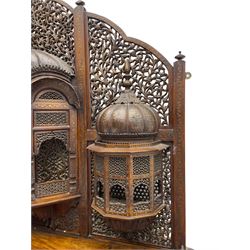 Late 19th century Indian Burmese carved and pierced hardwood and brass inlaid wall shelf, the shaped back profusely decorated with trailing and interlaced foliage, with projecting architectural structures, the central balcony with canopy top and five open windows with arched apertures on columns, two flanking five-sided balconies, the shelf supported by six foliate carved columns with pierced cusped pointed arches 