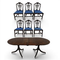 Set of six George III style mahogany dining chairs, comprising six singles with shaped top rail above pierced splay carved with feathers, with drop in stuffover seats upholstered in blue striped fabric, raised upon square tapering legs joined by stretchers, together with a mahogany twin pedestal dining table, the oval top with central leaf raised upon turned columns and splayed reeded legs terminating in lion paw feet and brass castors,