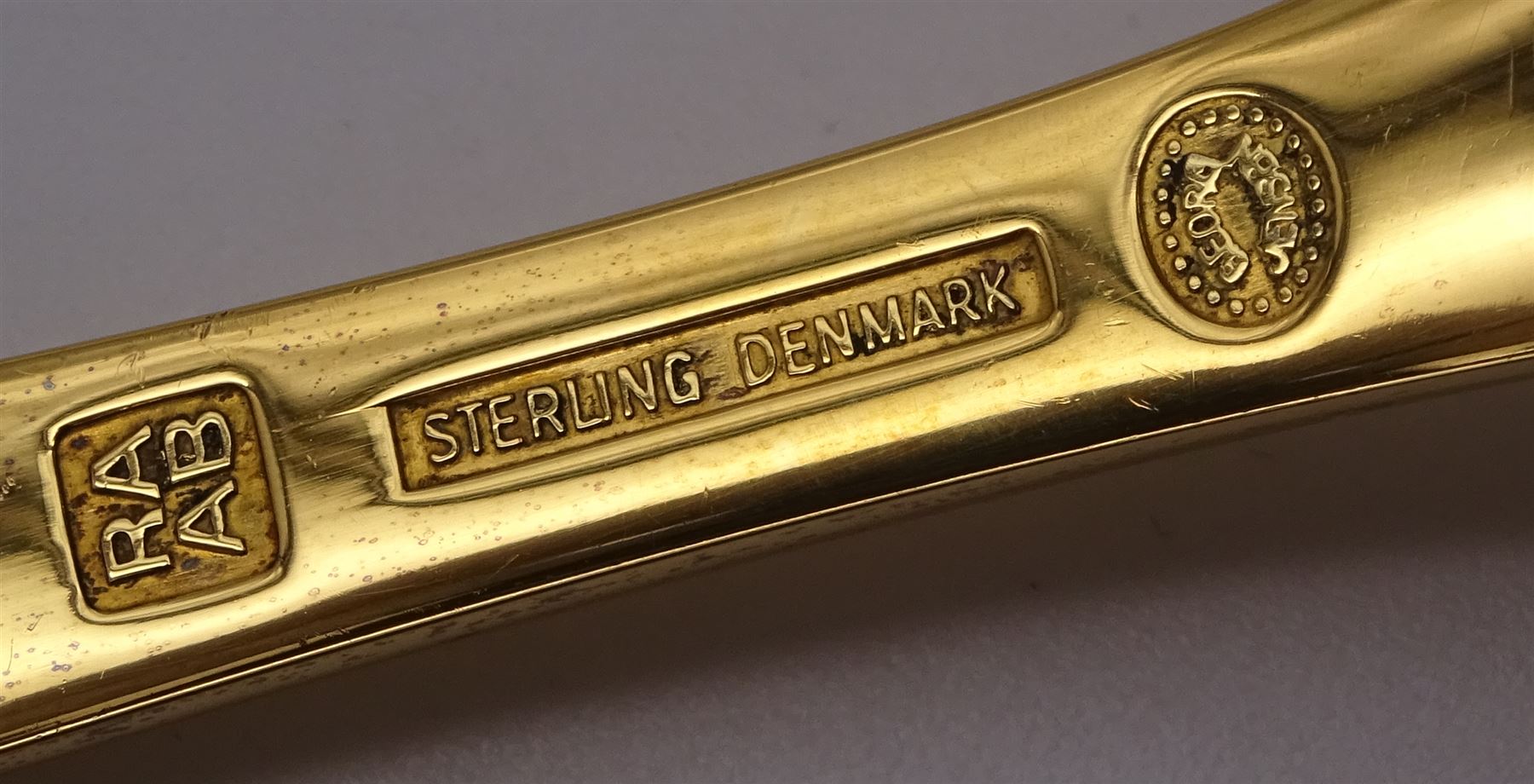 Two Danish silver-gilt year spoons by Georg Jensen, the first example decorated with enamel blue cornflower motif, dated 1972, in original pouch, the second example decorated with enamel pink briar rose motif, dated 1976, in original box, each impressed on underside RA AB, Sterling Denmark, and marked for Georg Jensen, together with two further examples by A.Michelson, the first with orange enamel fan design, dated 1965, impressed on underside A.Michelsen Sterling Danmark, TH, the second with enamel family scene, dated 1973, impressed on underside 925 S A.Michelsen Sterling Danmark, B Spang Olsen, approximate gross weight 6.11ozt (190.4 grams)