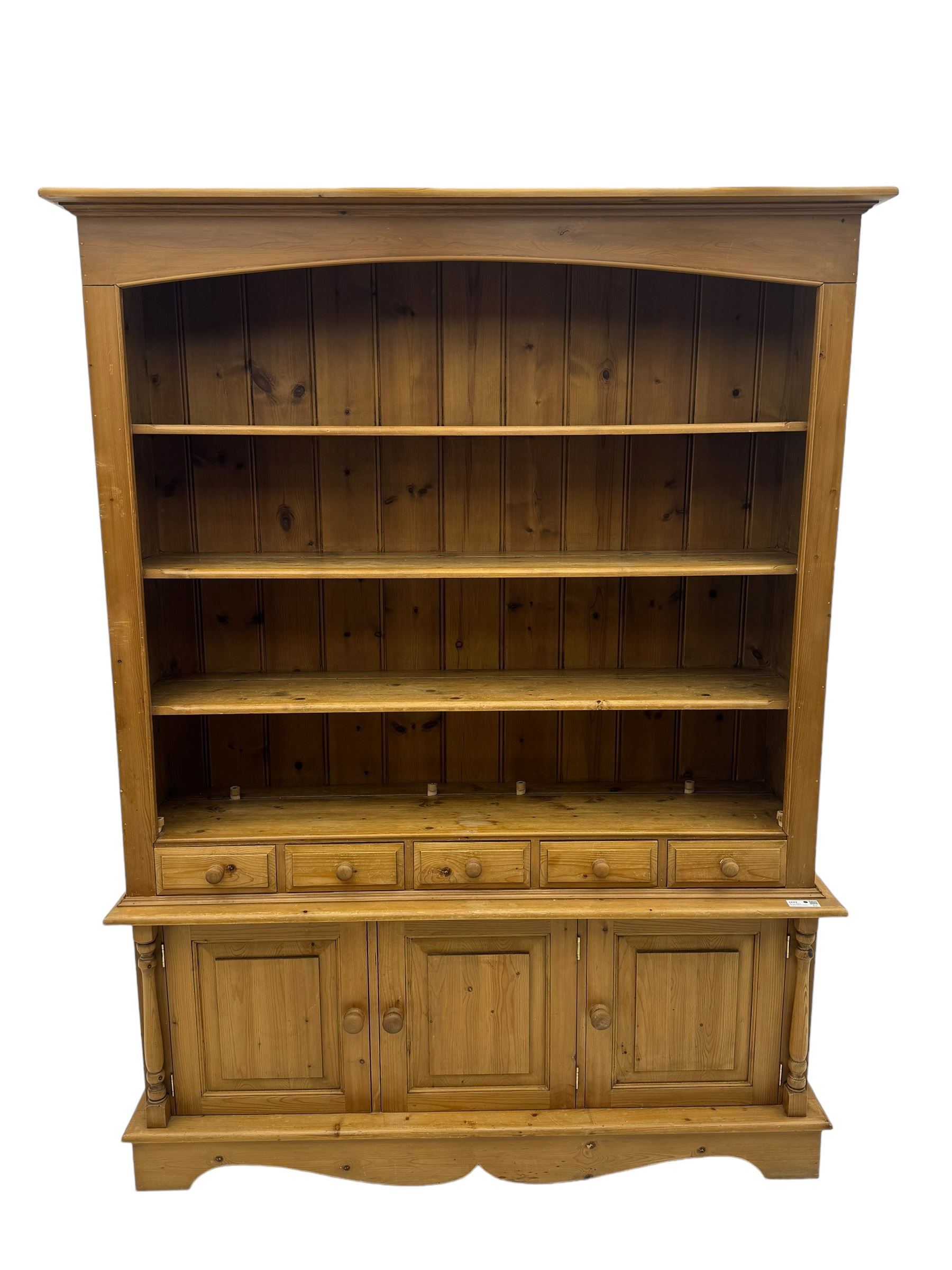Early 20th century pine kitchen dresser, featuring a hutch with arched top over three open shelves, the base with five drawers over three cupboard doors, turned column supports flanking the doors, scalloped apron base with bracket feet