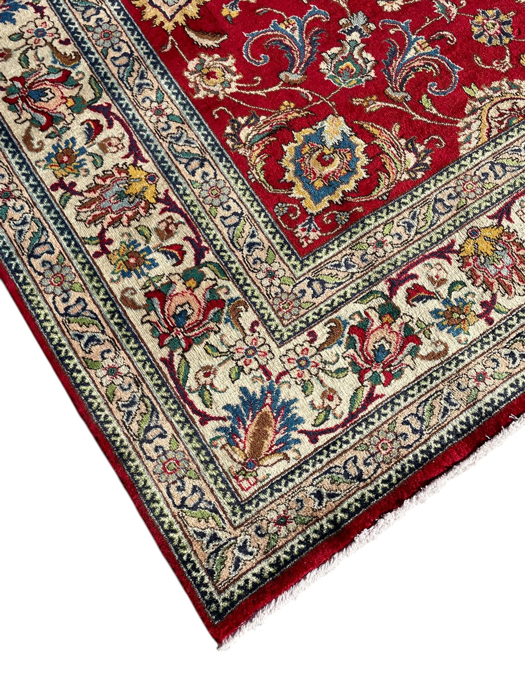 Persian Tabriz crimson ground carpet, decorated with swirling leafy branches and large palmette motifs, the pale ground border decorated with trailing foliate pattern, within floral guard stripes