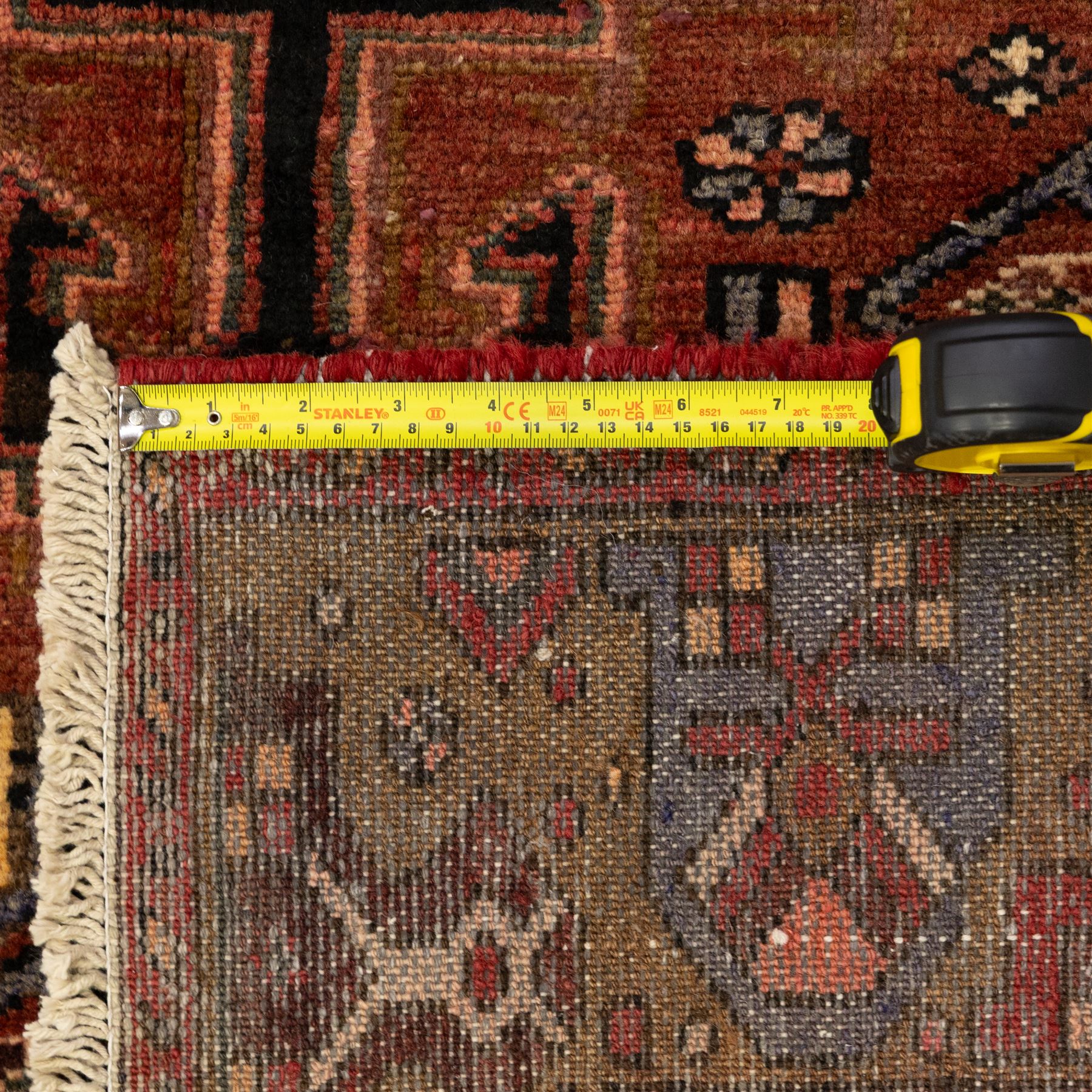 North West Persian Zanjan hand-knotted rug, madder-red field with a central stepped lozenge medallion enclosing stylized geometric floral motifs in indigo, ivory, and brown, angular spandrels filled with tribal devices and framed by a series of geometric borders with latch-hook rosette and leaf motifs, with cotton fringe ends  