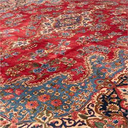 Fine Persian crimson ground Kashan carpet, the busy field with a central floral pole medallion surrounded by bouquets of flowerheads and trailing foliage, the shaped cyan spandrels similarly woven, enclosed by a wide foliate guard band of stylised palmettes and floral designs