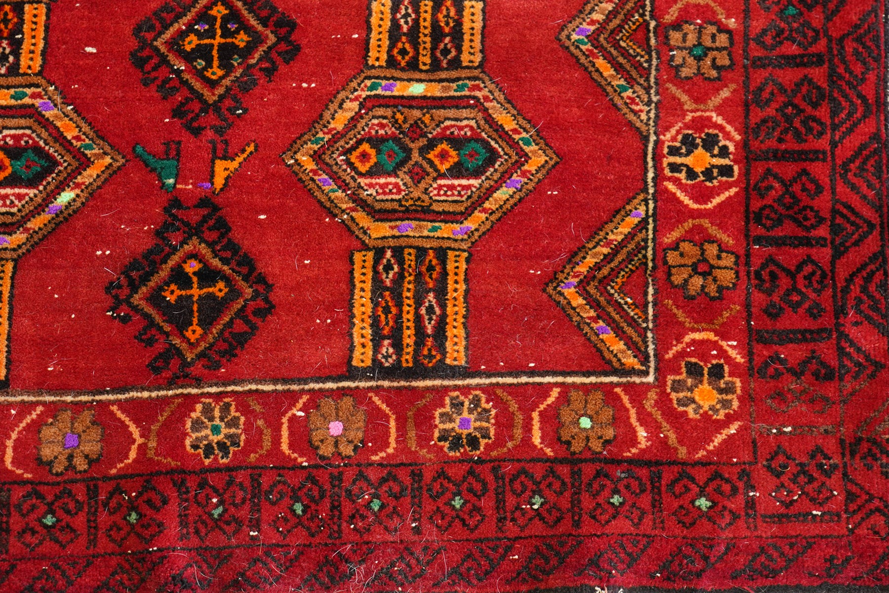 Persian Baluchi crimson ground rug, decorated with three columns of geomtric motifs