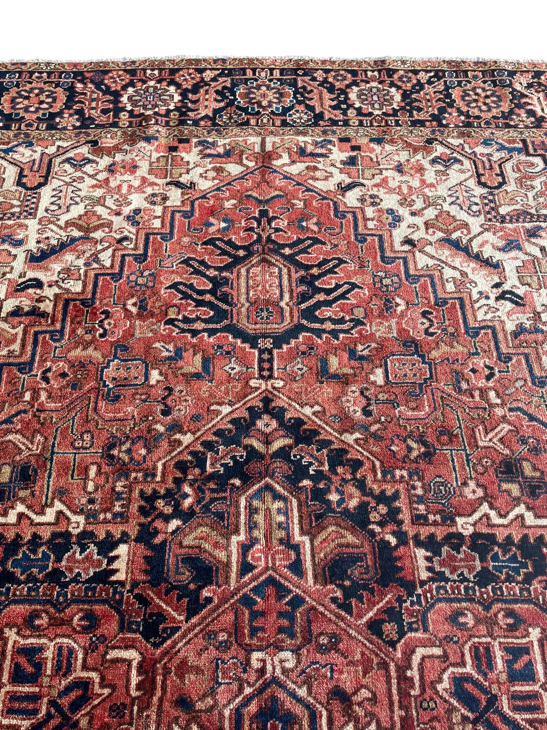 Persian Heriz red ground carpet, large stylised pole medallion surrounded by Pitrak motifs, indigo ground border decorated with stylised flower heads and trailing leafy branches, within floral pattern guard stripes