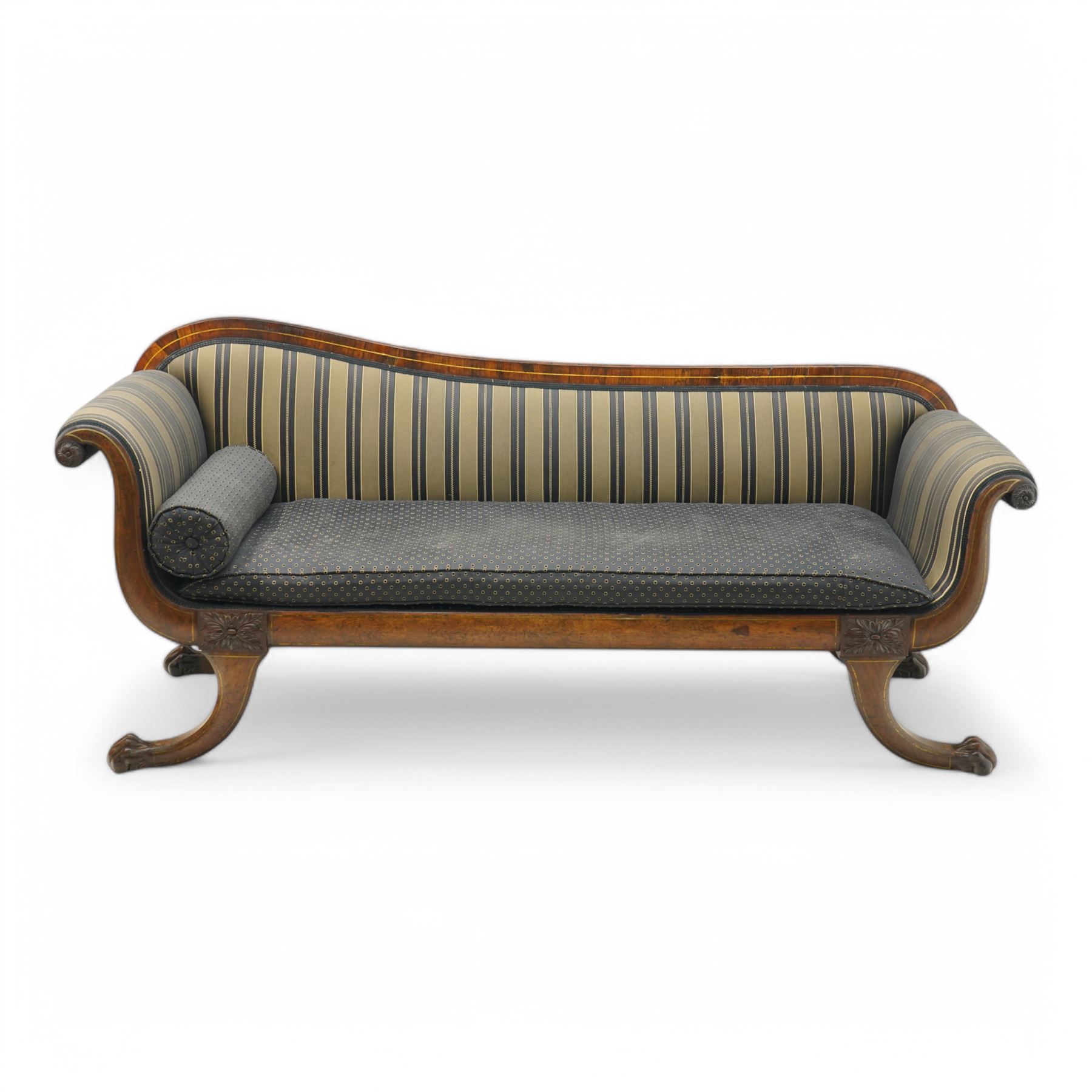 Regency brass inlaid rosewood chaise lounge or settee, shaped back over rolled head and foot, upholstered in black and gold striped fabric with rectangular squab cushion and bolster cushion, the rolled terminals carved with acanthus leaf roundels, lower rectangular foliate carved panels, on out splayed supports with paw carved feet 