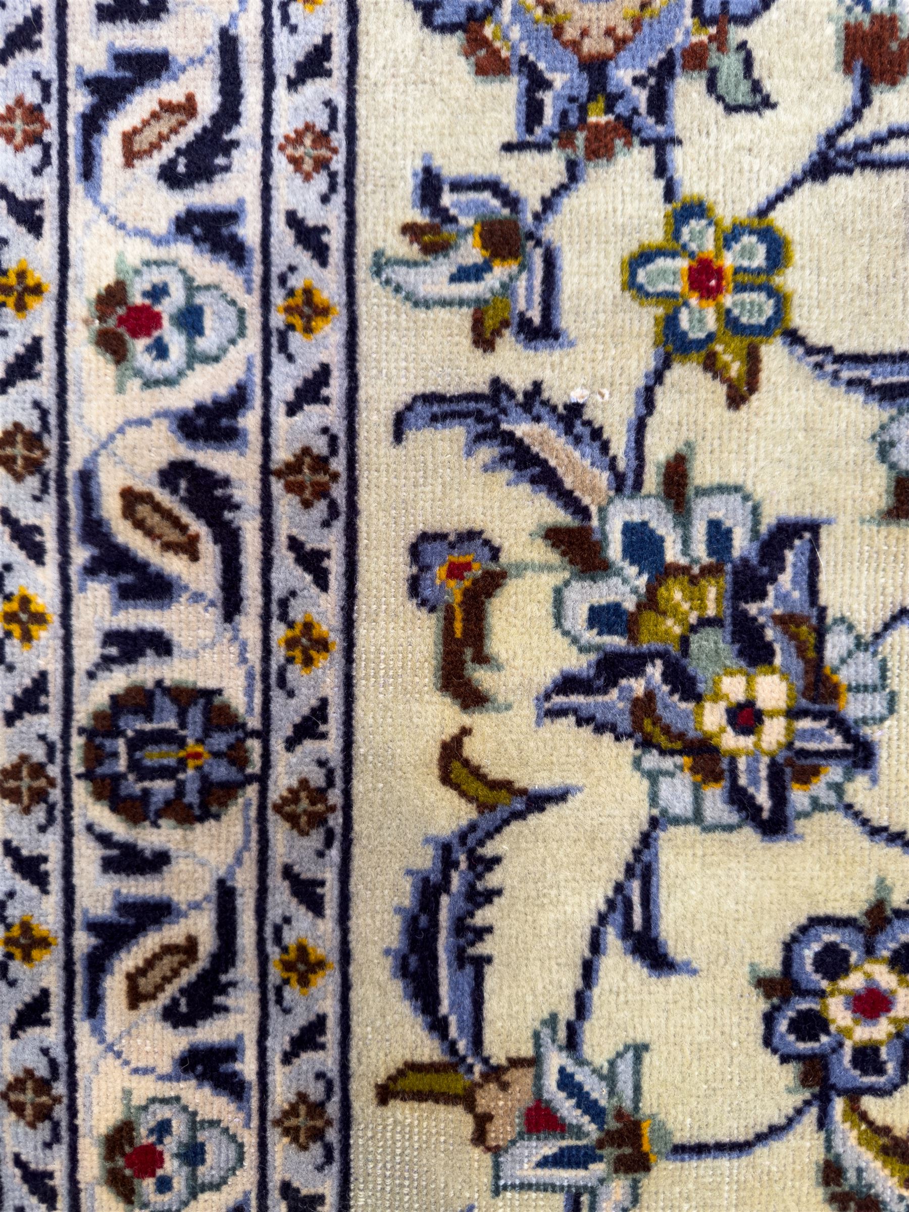 Central Persian Kashan hand-knotted carpet, ivory field with an all-over design of scrolling vines, lotus palmettes, and rosettes in shades of blue, gold, and brown within a blue ground border of palmettes and arabesques between multiple guard stripes