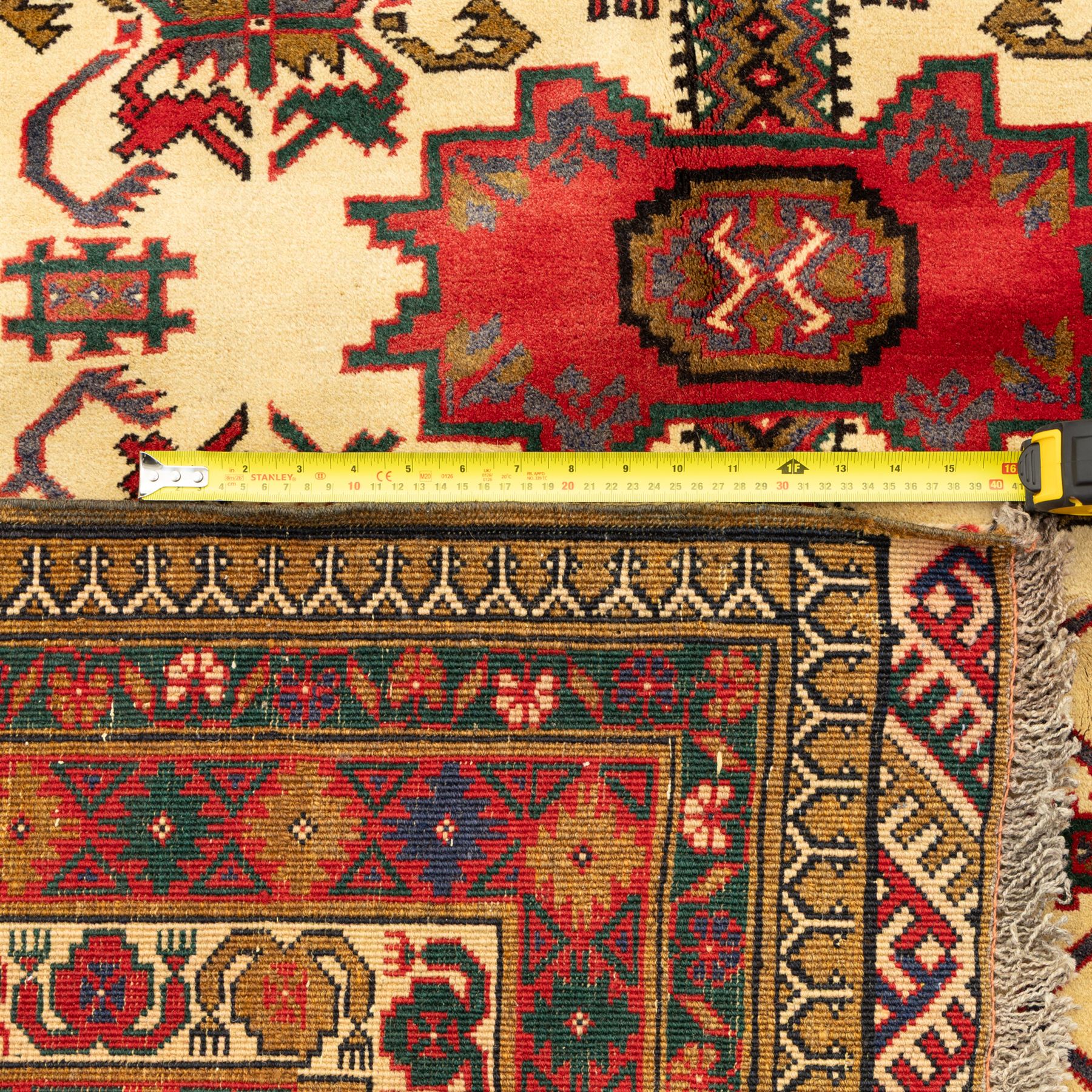 North East Persian Gochan hand-knotted rug, ivory field decorated with a vertical column of stepped polygonal medallions flanked by stylized geometric floral motifs enclosed by multiple borders incorporating rosette and reciprocal devices, in a palette of madder red, indigo, olive green, and aubergine, with cotton fringe ends  