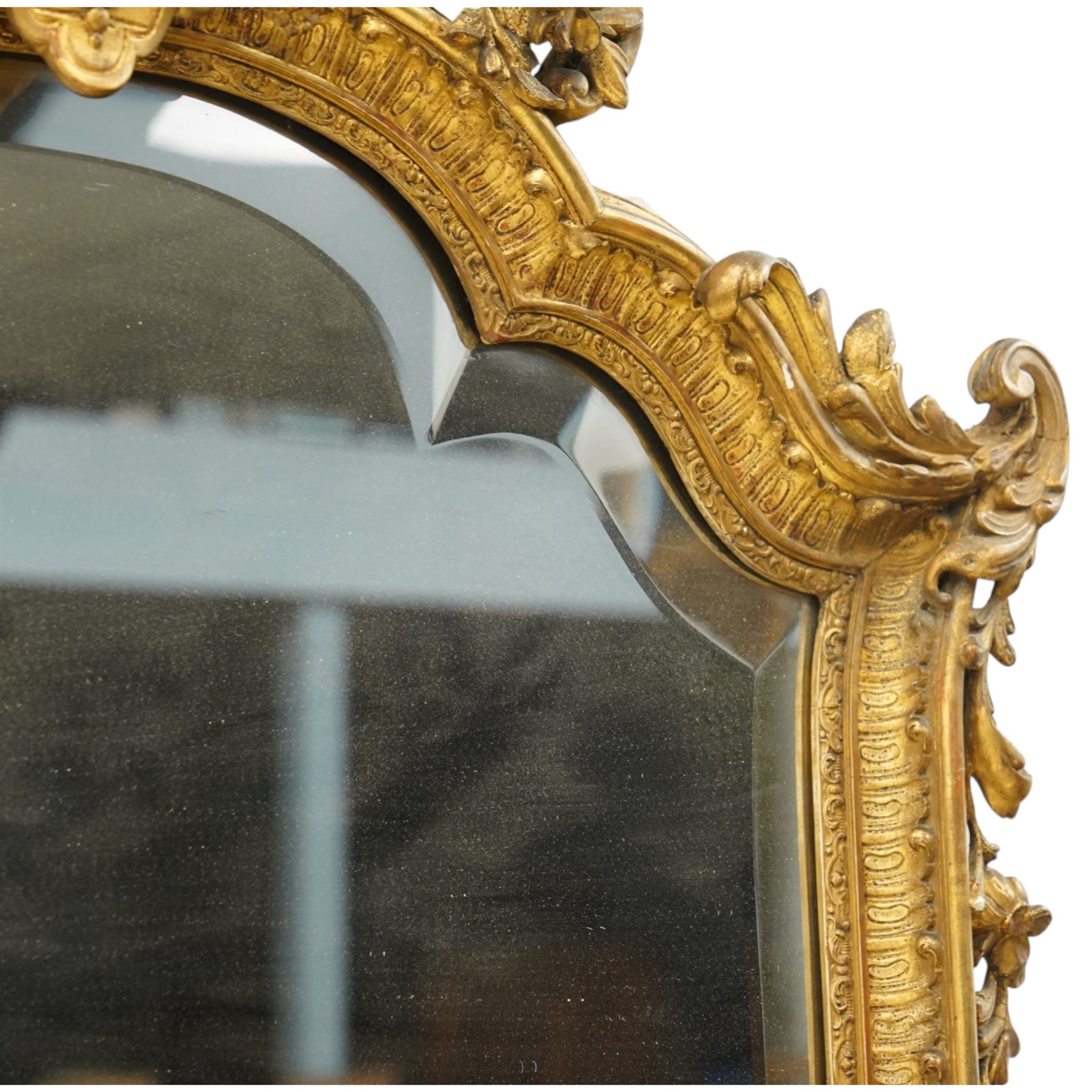 Victorian giltwood and gesso framed ornate wall mirror, the protruding cartouche pediment decorated with extending scrolls of acanthi and flower heads, with scrolled foliage corners flanking a carved slip with further gadrooned scroll decoration, contained a shaped rectangular bevelled plate, over a pierced and scrolling scallop shell terminal
