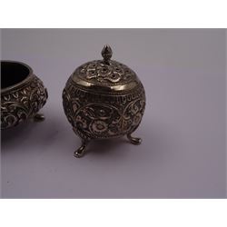 Indian silver pepper shaker, of spherical form, with embossed floral and foliate decoration, upon three pad feet, together with a similar Indian silver open salt and an Indian silver salt spoon with twisted serpent handle and shell bowl