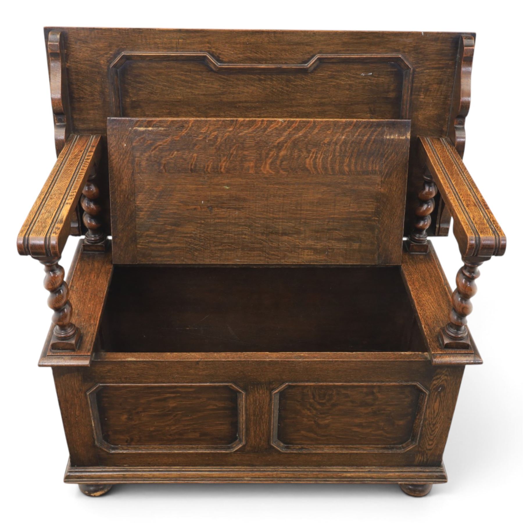 Early 20th century oak monks bench, panelled back converting to a table top, reeded armrests with barley twist uprights, hinged seat over panelled base supported on bun feet
