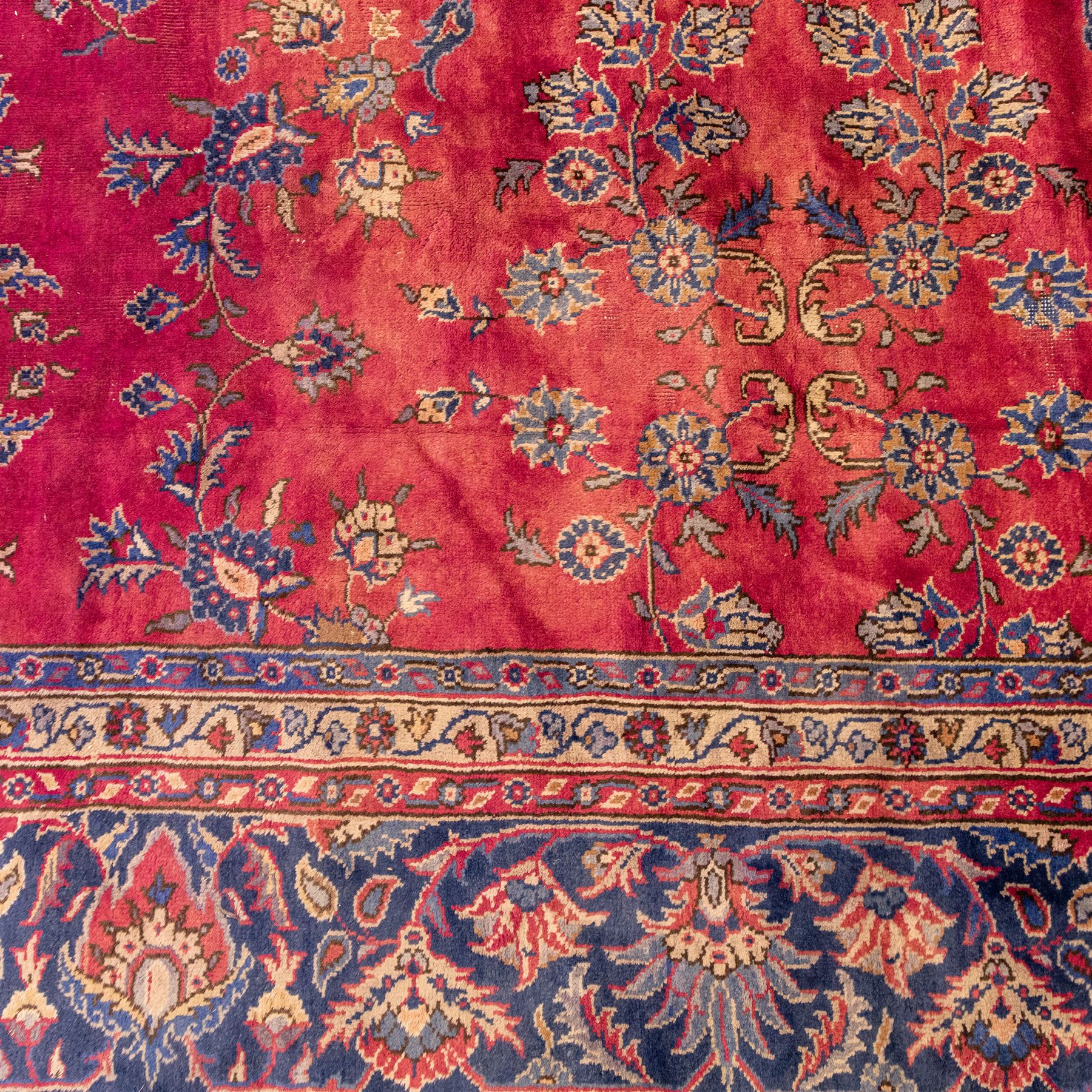 Large Persian-style mahal-type hand-knotted carpet, of rectangular form with a deep crimson field decorated with an all-over arrangement of stylized floral sprays and palmettes, with a central subtle medallion composition enclosed by a dark navy main border of scrolling floral motifs between narrow guard stripes with fringe ends 