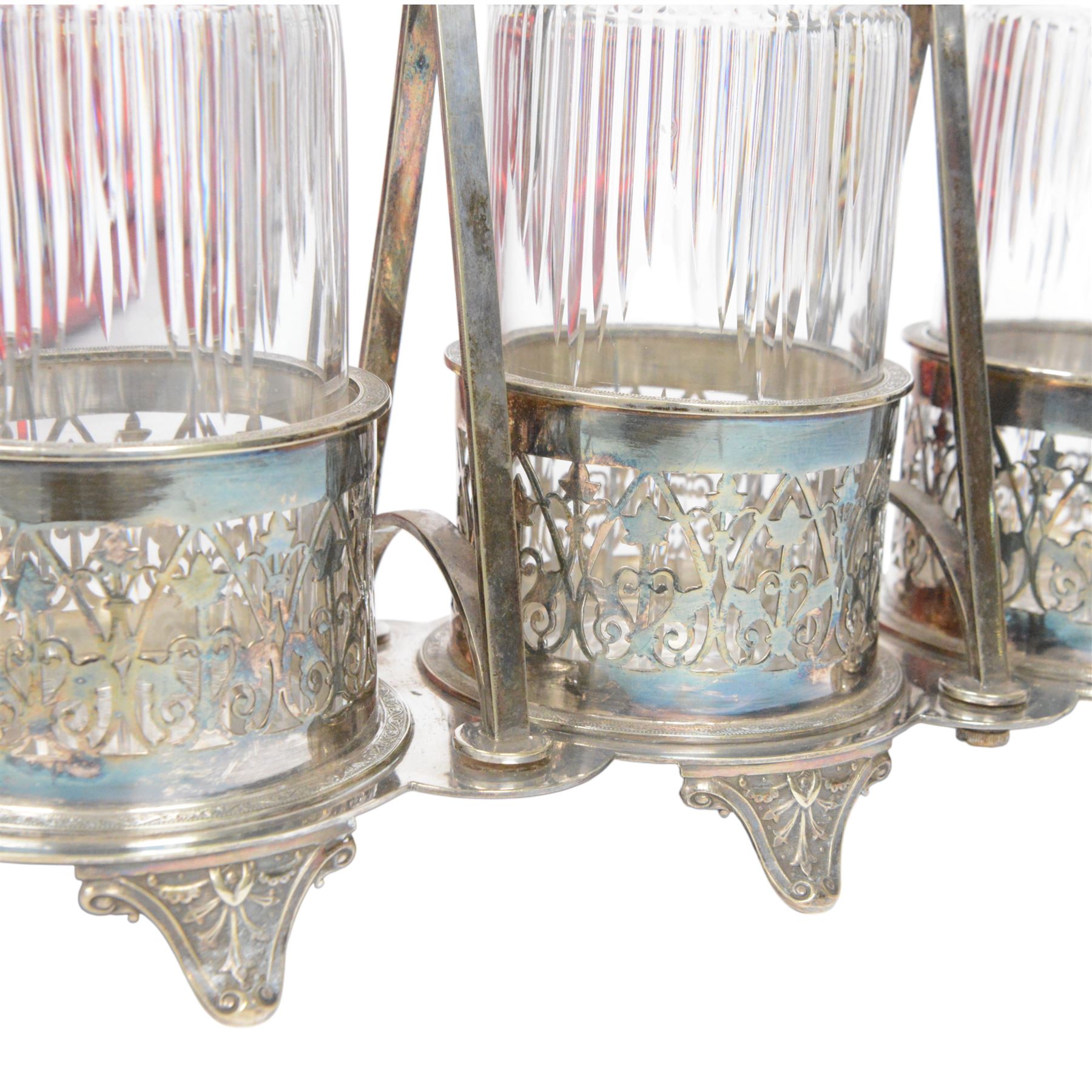 Late 19th century silver plated Silber & Fleming triple decanter stand, the three cut glass decanters with spire stoppers housed within foliate and scroll pierced bottle sleeves, upon a tripart base with six scroll feet, the base mounted with articulated x-frame curved handle, including handle when positioned upright H35.5cm, W34cm