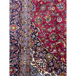 Central Persian Kashan hand-knotted carpet, the madder red field with central lobed medallion in indigo and ivory, enclosing scrolling arabesques and flowerheads, framed by palmette spandrels and an indigo border of rosettes and lotus forms between multiple floral guard stripes, from the region of Kashan