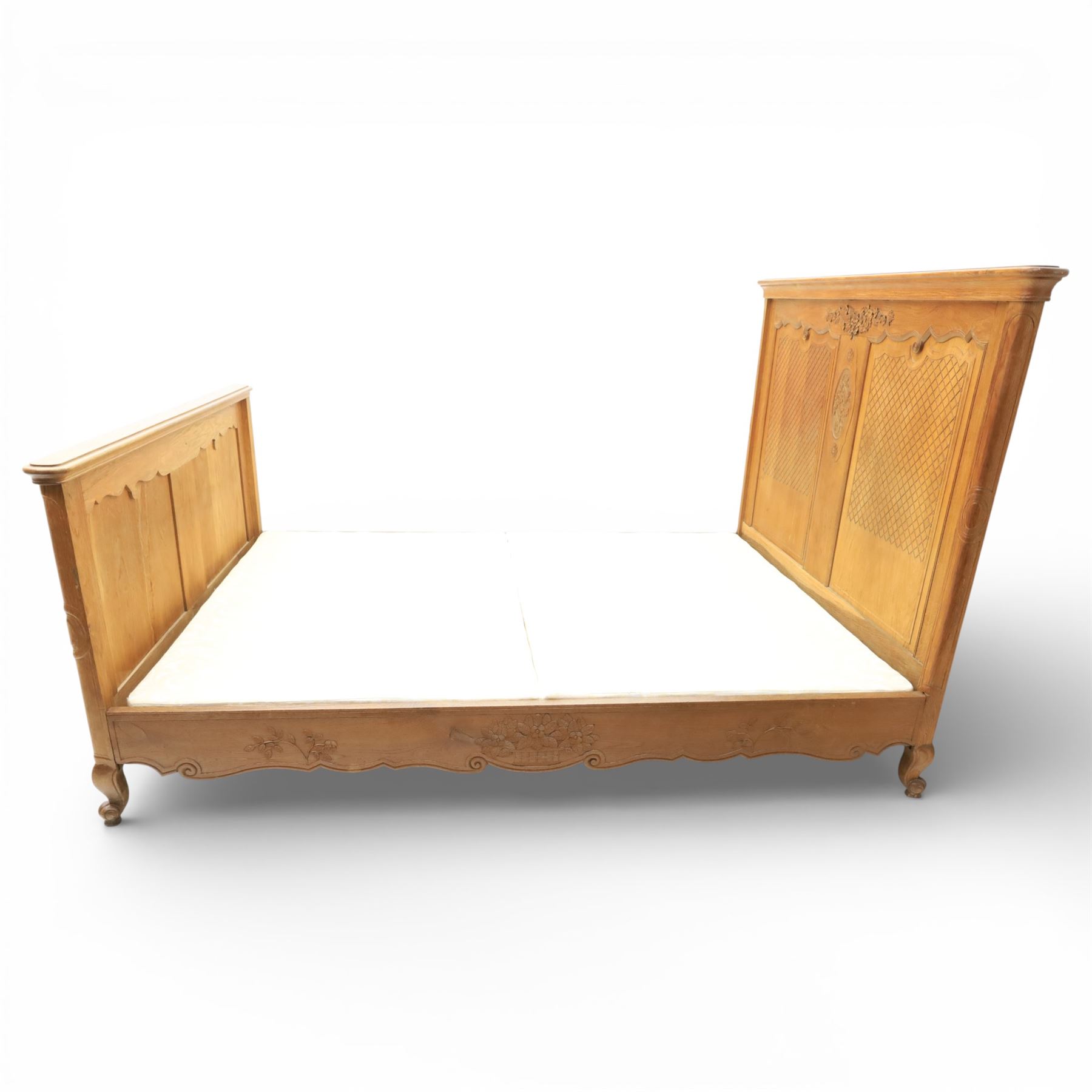 Early 20th century French oak double bedstead, the shaped and moulded headboard carved with central floral cartouche and scrolling foliage above lattice carved panels, the conforming footboard with pierced and carved decoration, shaped apron with foliate carving, raised upon cabriole supports