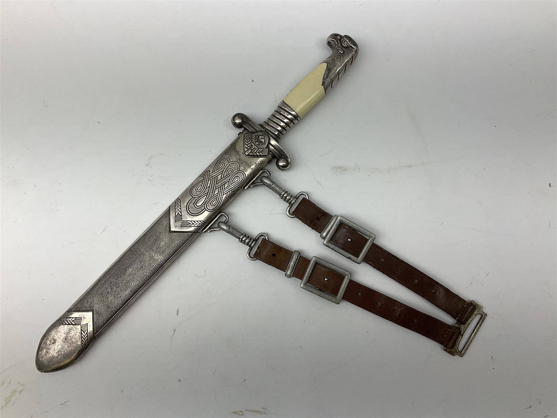 German Reichsarbeitdienst RAD Leader's Hewer dagger, the 26cm single edged scimitar shaped blade with narrow fuller, etched Arbeit adelt; by E.D. Wusthof, Solingen; the aluminium hilt with spade and wheat ear langet; two piece white plastic grip and eagle head pommel; pebbled steel scabbard engraved with ears of wheat and strapwork with double leather hangers L40cm overall