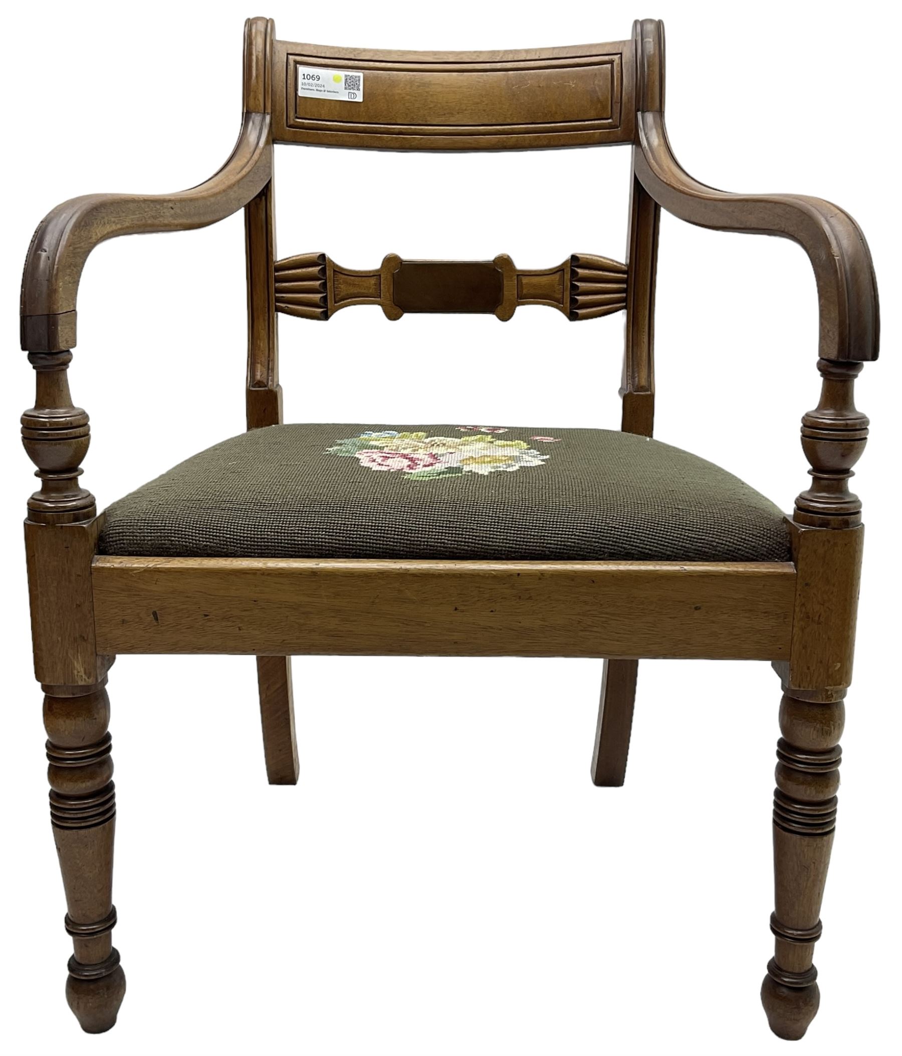 Regency mahogany elbow chair, carved shaped central back bar, over drop-in seat upholstered in floral needlework, raised on ring turned front supports