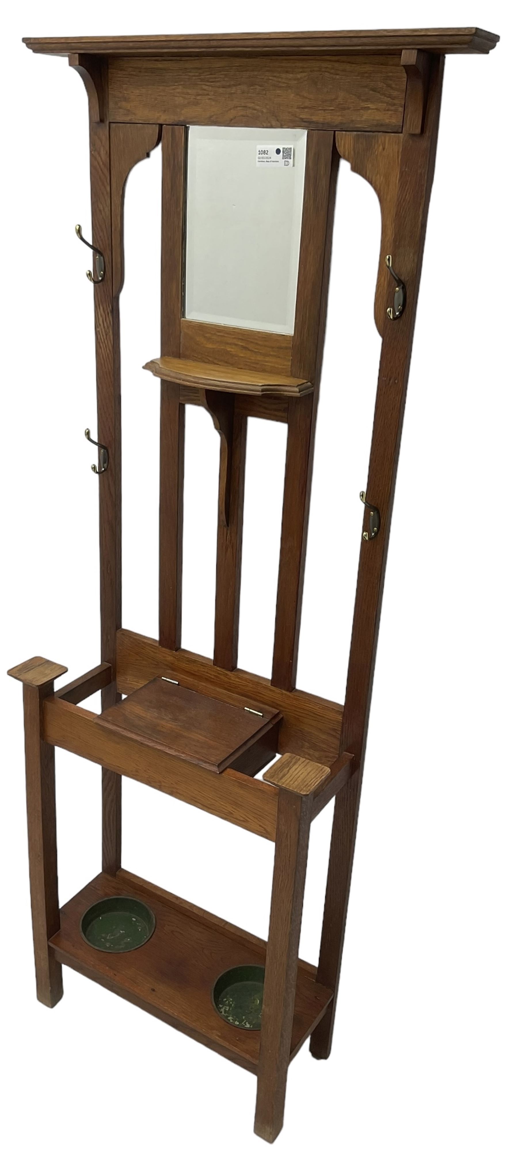 Edwardian oak hall stand, raised back with rectangular bevelled mirror plate surrounded by shelf and coat hooks, fitted with a glove box with hinged lid, over an undertier with two inset umbrella drip trays