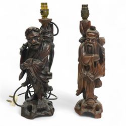 Two of Chinese hardwood table lamps, carved as two elderly figures, the first holding a bi...
