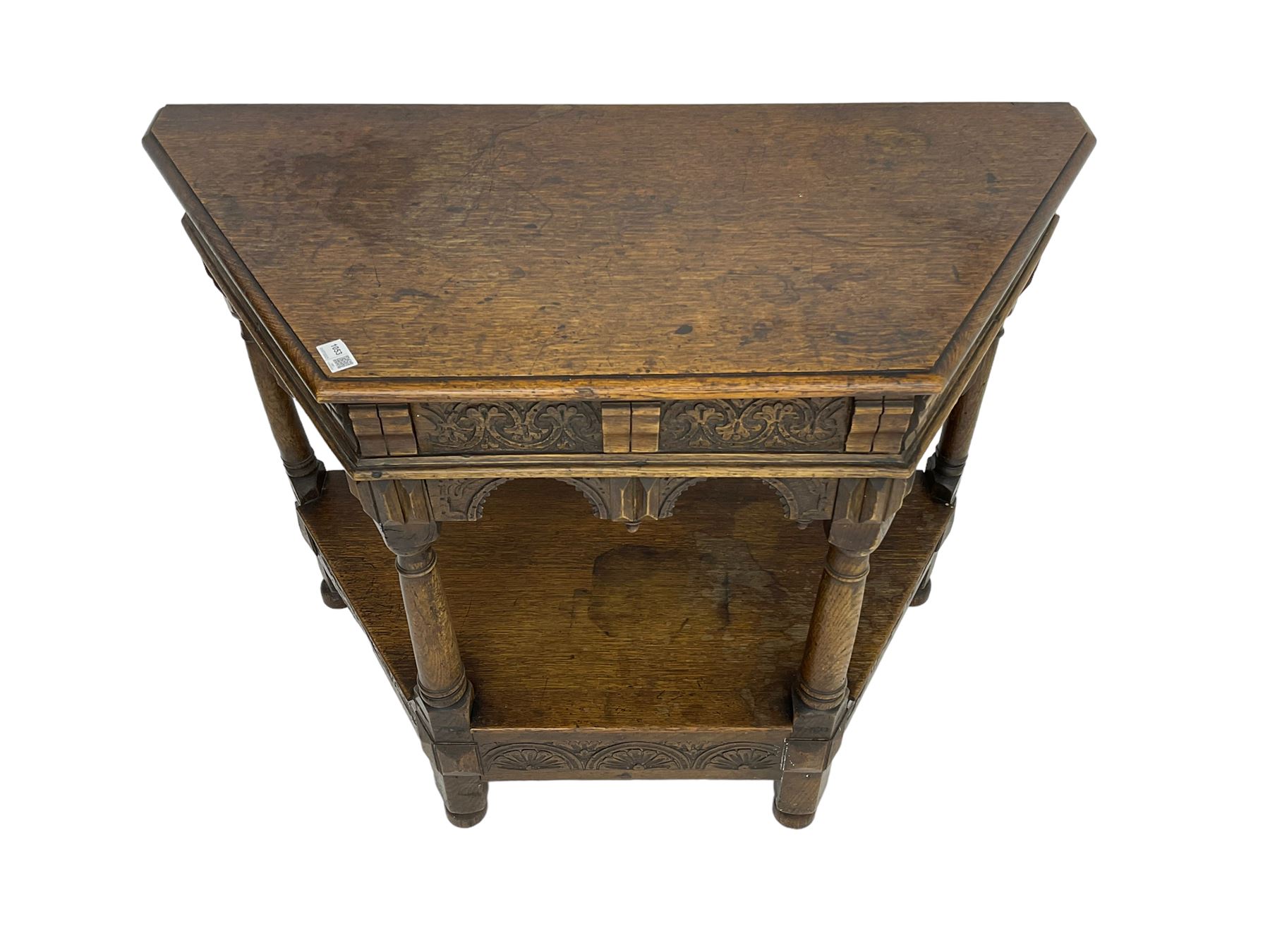 Jacobean design carved oak side or credence table, demi-heptagon top with moulded edge, frieze carved with foliate C-scroll design above ornate arcade carved apron, under-tier united by ring turned pilisters, lower frieze carved with repeating lunettes
