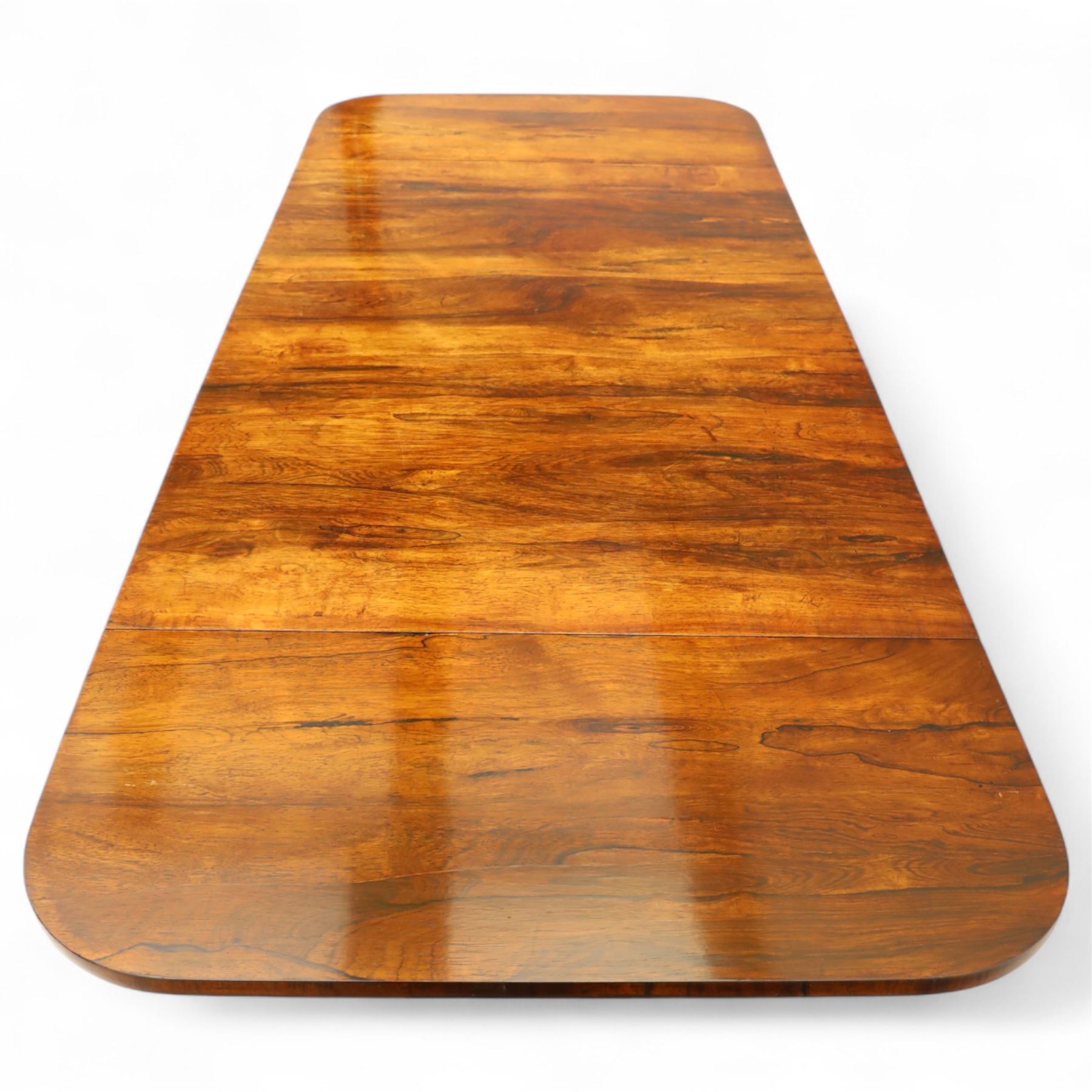 Regency rosewood sofa table, rectangular top with variegated rosewood veneers, hinged D-shaped leaves, over a set of dummy drawers to the back and full-size drawers to the front, with turned knob handles and gilt beaded moulding on frieze above elegant turned, tapering, and fluted, pedestal with a well-carved collar, supported on a large, tripartite concave platform base terminating in richly carved lion paw feet with gilded acanthus leaf carving, on concealed brass castors, circa 1815, length extended 161cm 
