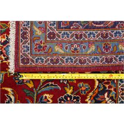 Central Persian Kashan hand-knotted carpet, crimson field with central cusped medallion in ivory, pale blue and indigo, issuing a network of scrolling arabesques, palmettes, and floral sprays, with conforming spandrels, main border of scrolling vinery and stylized palmettes, framed by multiple guard borders, with cotton fringe ends 