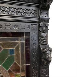 19th century heavily carved and stained oak cabinet on cupboard, the projecting moulded cornice over gadroon carved frieze, the upper cabinet enclosed by stained and leaded glass door in geometric pattern with central star motif, in various coloured and textured glass panes, the upright rails carved with flower heads and the panelled back carved with circular motifs behind turned supports, moulded rectangular top over frieze drawer and cupboard, the cupboard enclosed by panelled door carved with Flemish design tavern scene, moulded skirted base on block feet