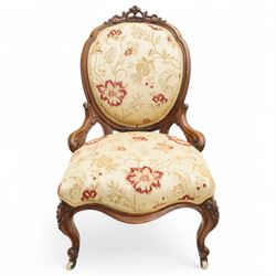 Victorian Ladies and Gentleman's carved walnut drawing room chairs, each with shaped cresting rail carved with scrolls and flowerheads, upholstered in pale gold floral fabric, raised on foliate-carved cabriole supports terminating to brass and ceramic castors