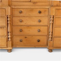 Large Victorian stripped pine reverse breakfront housekeeper’s cupboard, the moulded cornice above a central pair of panelled cupboard doors flanked by single cupboard doors and divided by turned baluster pilasters, the lower section fitted with an arrangement of twelve drawers with knob handles, raised upon bun feet