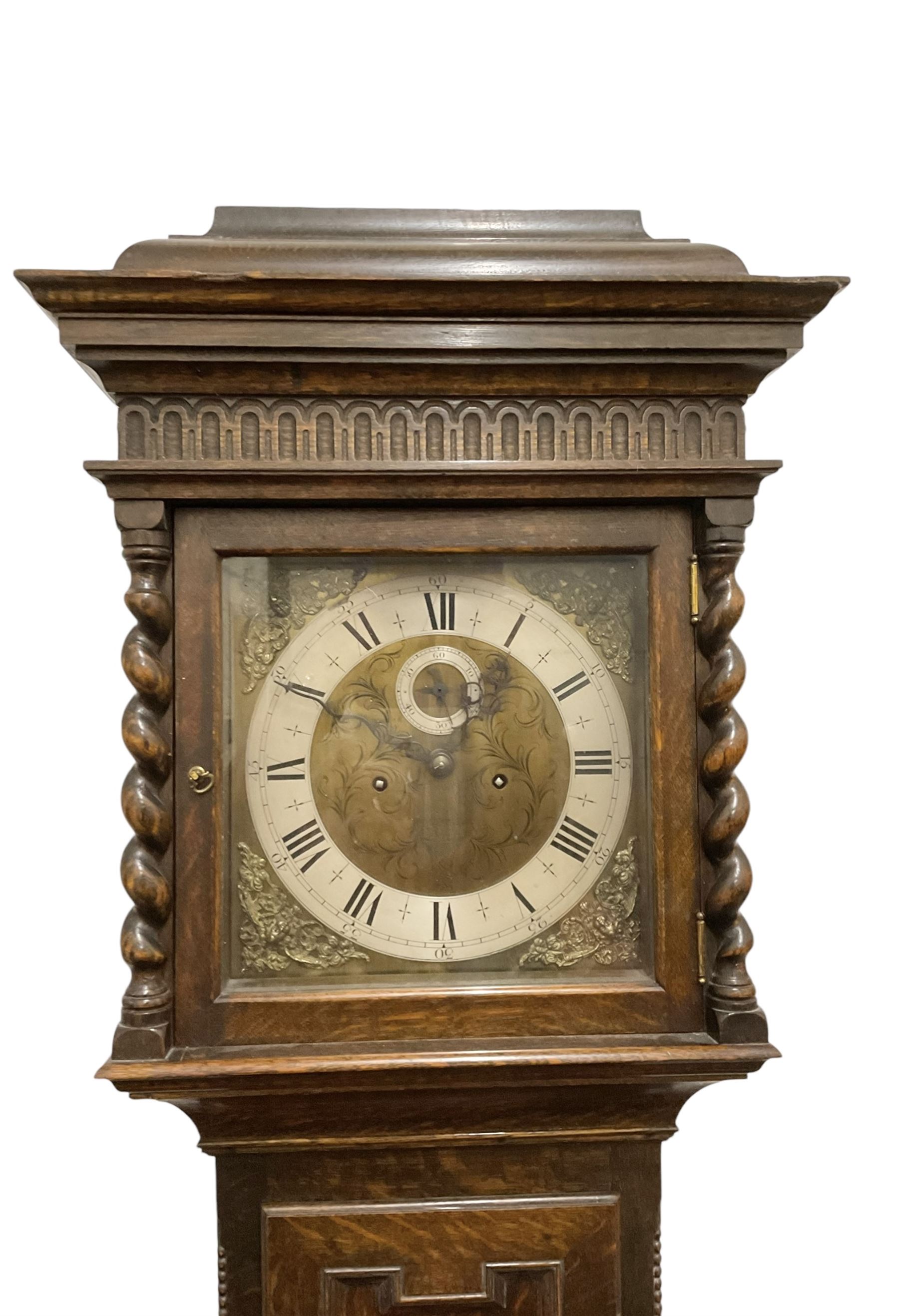 8-day oak longcase clock - in an early 18th century styled case with a caddy top, square hood door with barley twist columns, long carved trunk door on a conforming plinth with an applied skirting base, square brass dial with an engraved centre, silvered chapter and spandrels, 19th century rack striking movement, striking the hours on a bell. With weights and pendulum.