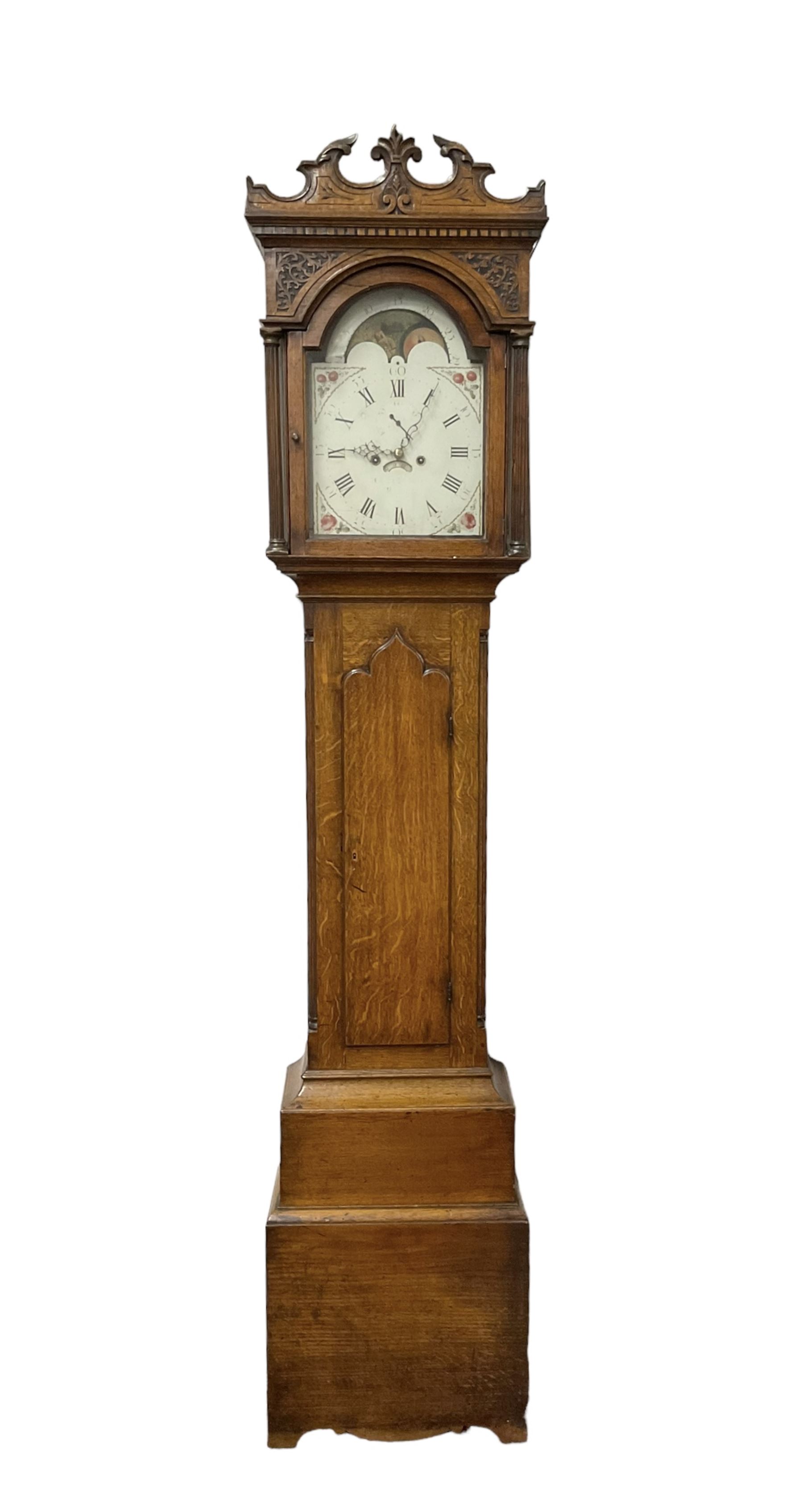George Clapham of Brigg - Late 18th century 8-day oak cased longcase clock c1790 - flat topped hood with later carved addition, dog tooth moulding and blind fretwork beneath, break arch hood door flanked by reeded pilasters and capitals, trunk with canted corners and  door with a triple arched top, plinth with a later base with decoratively shaped feet, early painted dial with flowers enclosed in a gesso border to the spandrels, rolling moon to the arch, seconds dial and calendar aperture, Roman numerals and five minute Arabic's with makers name (indistinct), dial pinned via a false plate to a rack striking movement. With weights, key and pendulum.