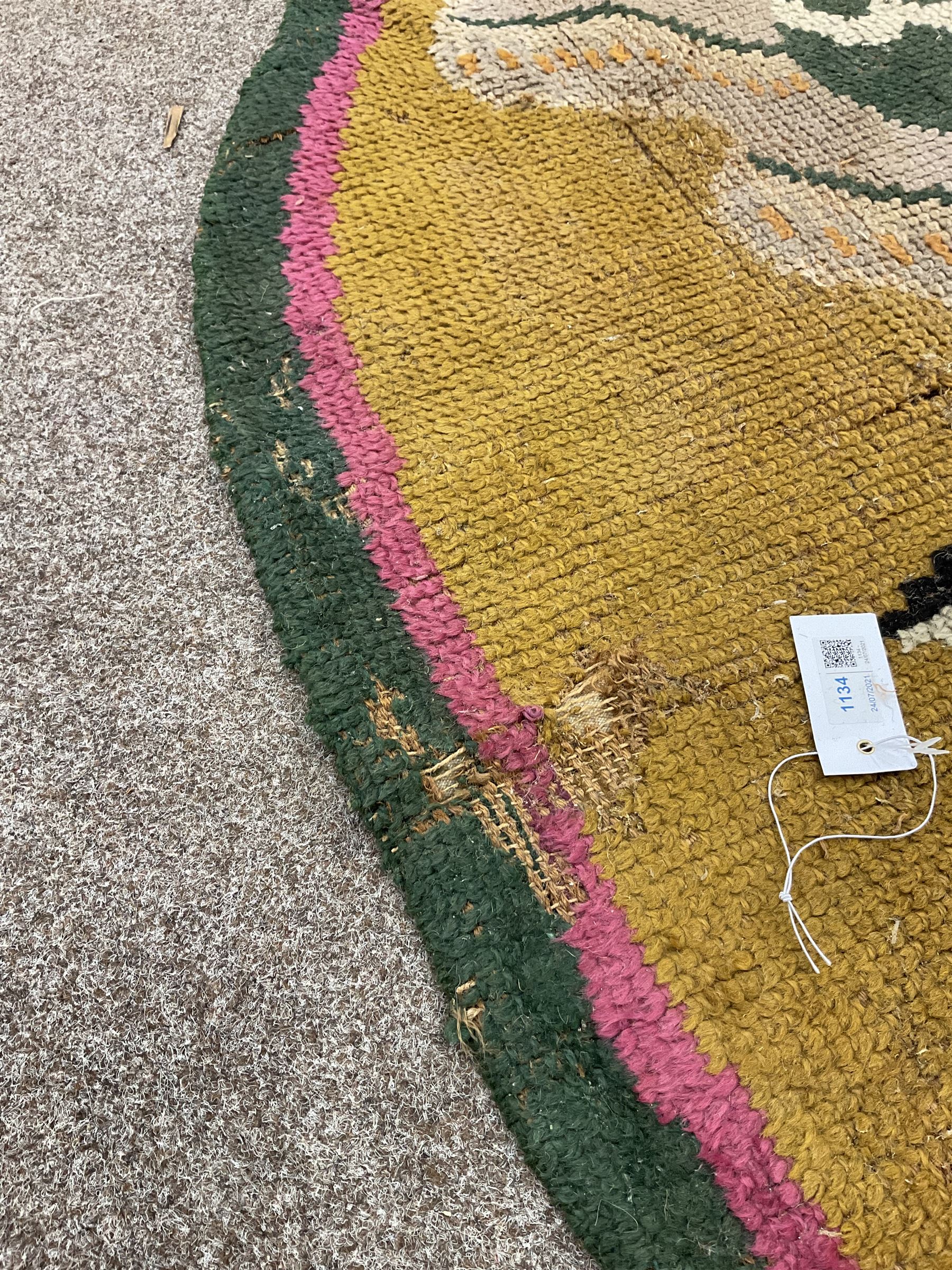 20th century wool oval rug, mustard ground and decorated with flower heads, with pink and green outer bands