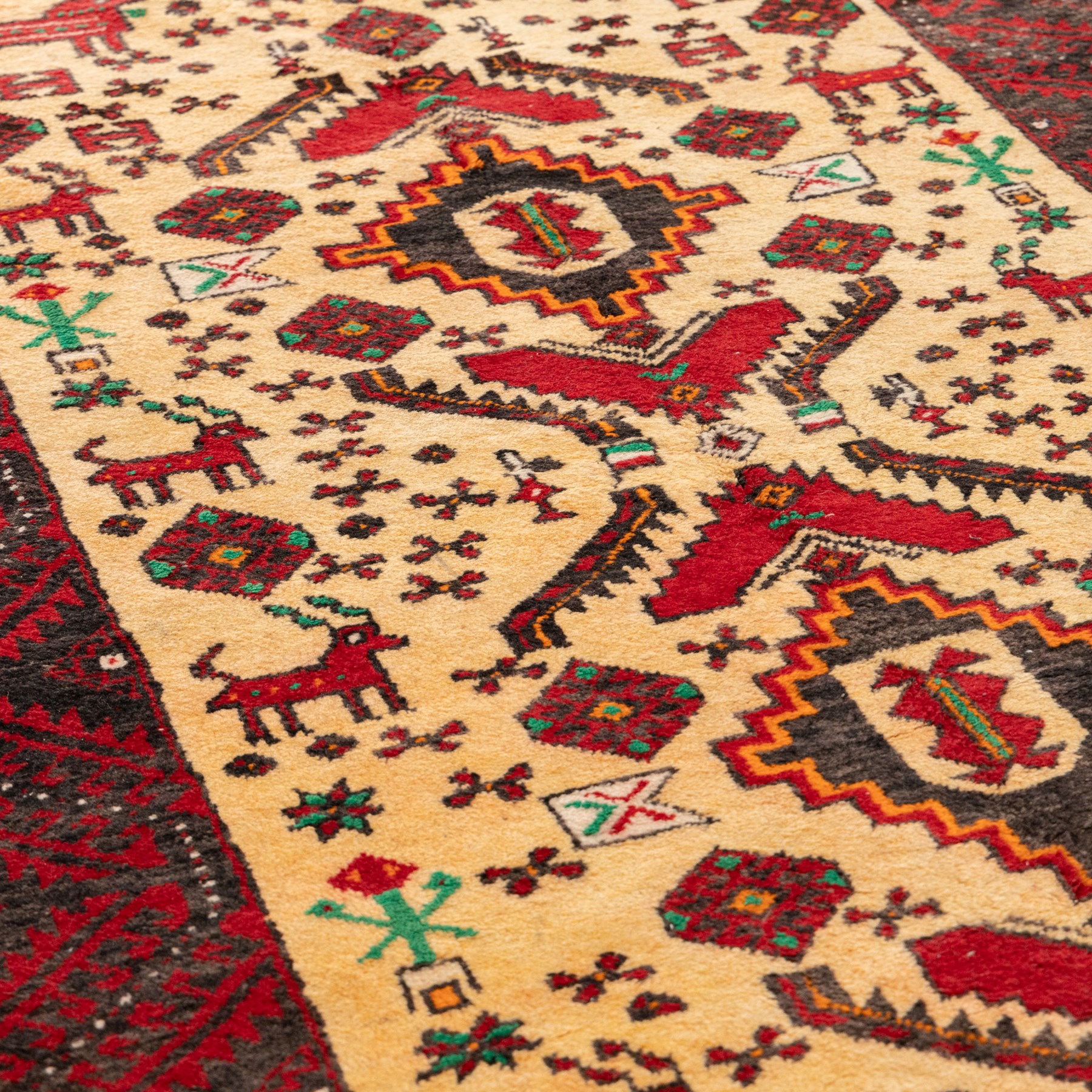 North East Persian Meshed Baluch rug, the ivory field decorated with two stepped diamond medallions and angular red motifs, interspersed with stylised horned animals, birds, flowerheads and geometric devices, enclosed by a dark brown border of repeating red serrated leaves and narrow ivory guard bands