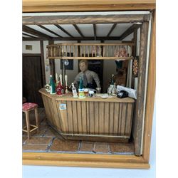 Dolls house scale room setting of a public house bar with tiled floor and beam and plaster ceiling and walls, bench seat, stools and table set out with a meal and drinks, large planked finish canted bar well stocked with food, drinks, bottles, glasses etc and bartender figure behind; electrically illuminated with sliding perspex access panel to front W38cm D28cm H24cm
