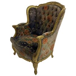 Pair of Louis XVI design gilt framed wingback armchairs, cresting rail carved and moulded with foliate decoration and C-scrolls, upholstered in buttoned floral patterned mauve velvet with loose seat cushion, scallop carved apron over cabriole supports