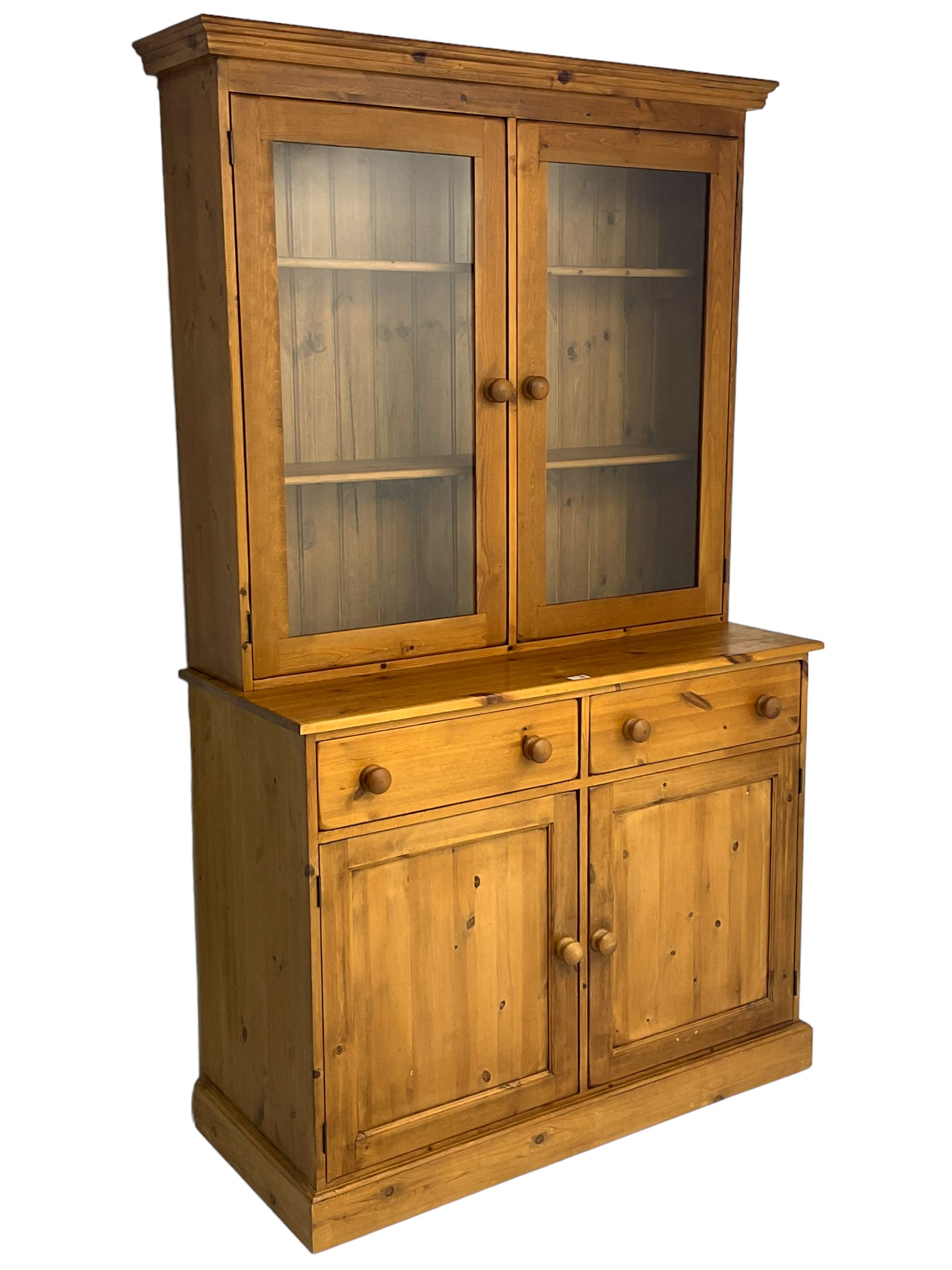 Large pine bookcase on cupboard, the upper section enclosed by two glazed door, the lower section fitted with two drawers and double cupboard, on plinth base