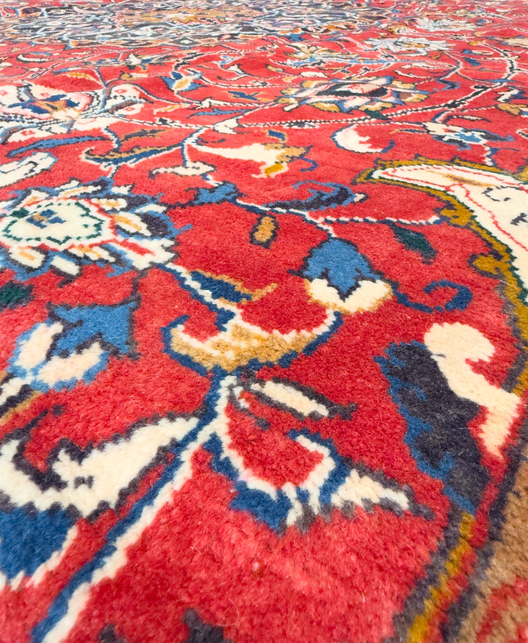 Northwestern Persian Lillihan hand-knotted carpet, madder red field with scrolling vines, rosettes, and palmettes around a central circular medallion in navy, ivory and ochre, and ivory ground spandrels within a navy border of stylized flowerheads and vines between multiple guard stripes 