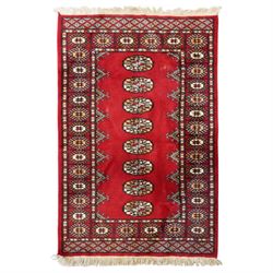 Afghan Bokhara crimson ground carpet, the field decorated with eight Gul motifs with surro...