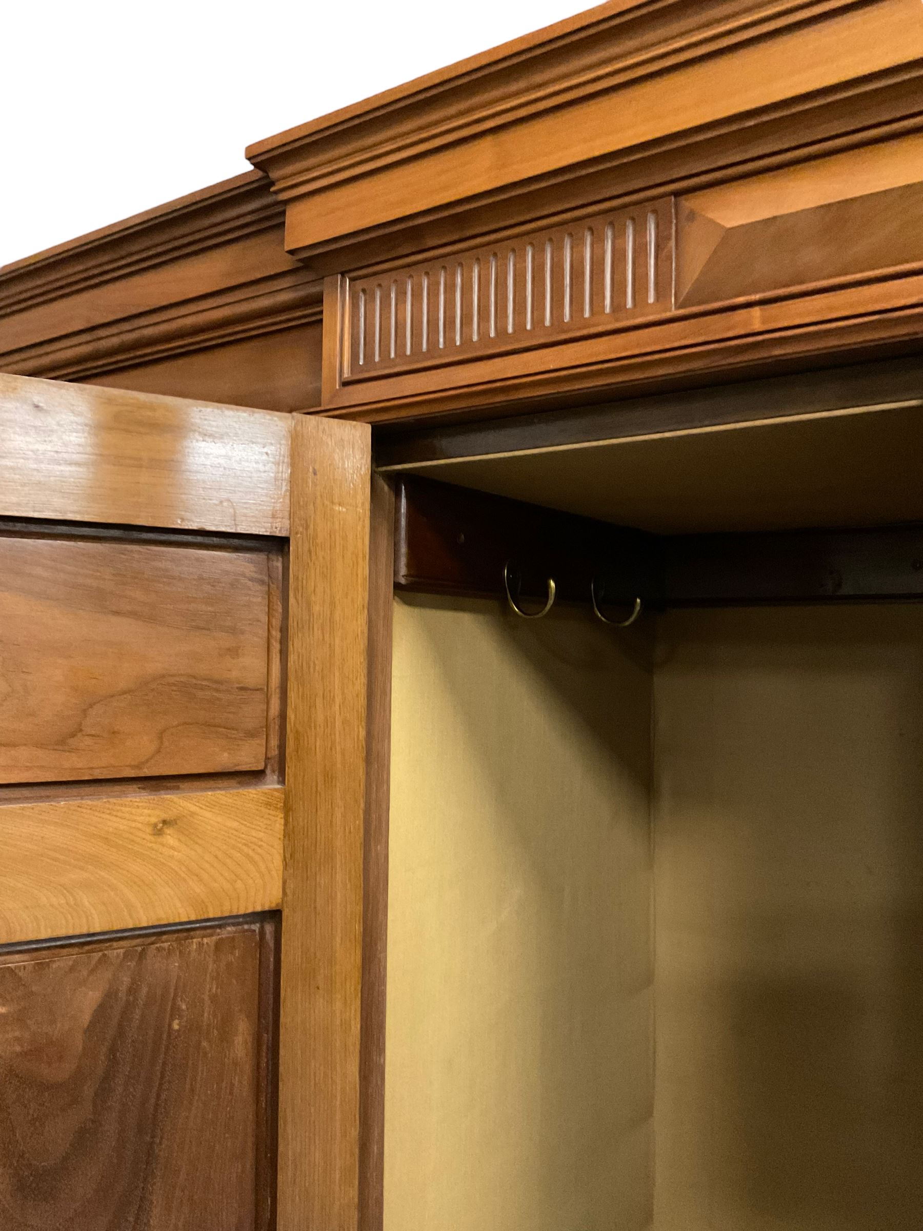 Edwardian walnut combination breakfront triple wardrobe, projecting cornice over cushioned and fluted frieze, central fielded panelled cupboard carved with foliate decoration above two short and three long drawers, flanked by two bevelled mirror doors enclosing hanging hooks with single drawers to base, retailed by J Tonks & Sons, Scarborough