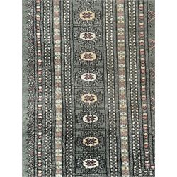 Pakistani Bokhara green ground rug, the field decorated with rows of repeating gul motifs, the main border featuring a series of smaller gul designs and geometric patterns, framed by multiple guard stripes