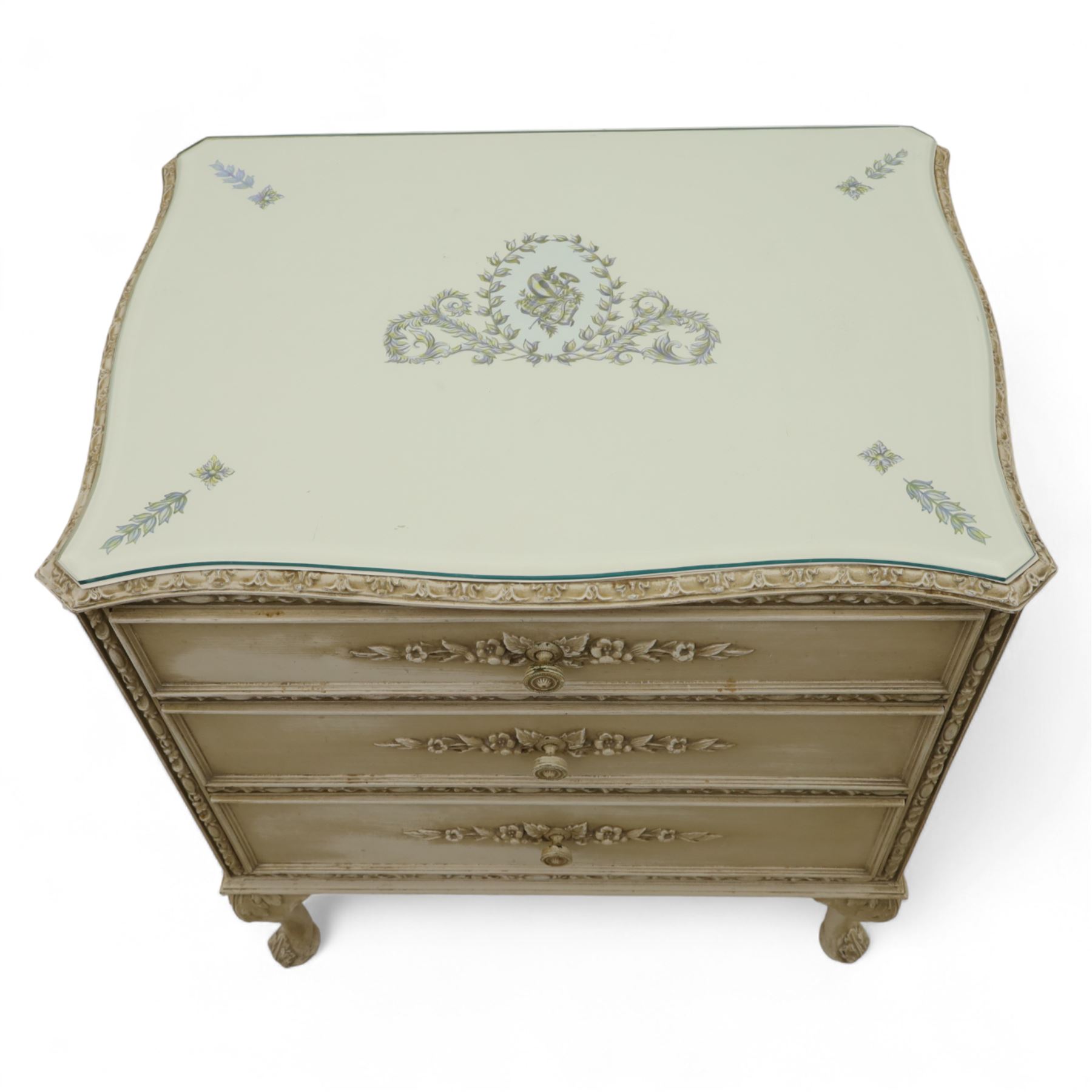 French design cream painted three drawer commode, shaped front with floral garland appliqués, fluted uprights and acanthus carved cabriole legs terminating in scroll feet