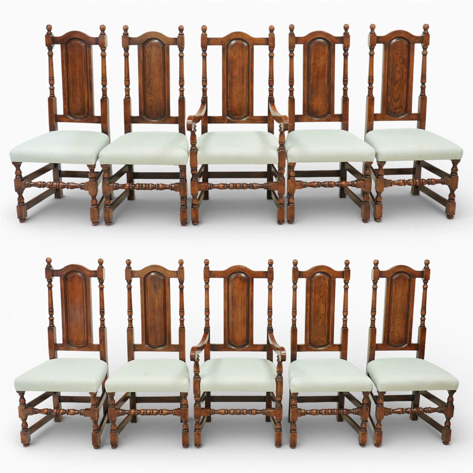 Country House oak high back dining chairs, set of ten comprising eight side chairs and two carvers, each with arched top rail flanked by turned finials over a central fielded panel back, with overstuffed seats upholstered in pale fabric, raised on turned front supports united by stretchers