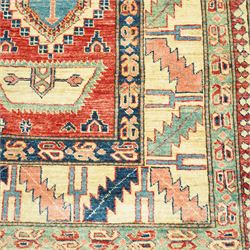 Caucasian Kazak hand-knotted rug, madder red field with bold geometric medallions and angular tribal motifs, within multiple patterned borders in a palette of indigo, red, ivory and green 