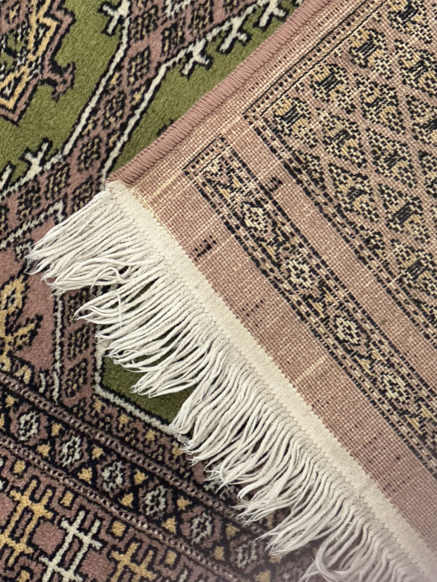 Pakistani olive and rose ground runner rug, the field decorated with repeating hexagonal medallions, surrounded by a rose-hued field with repeating diamond patterns, the borders featuring geometric motifs and trailing foliate designs