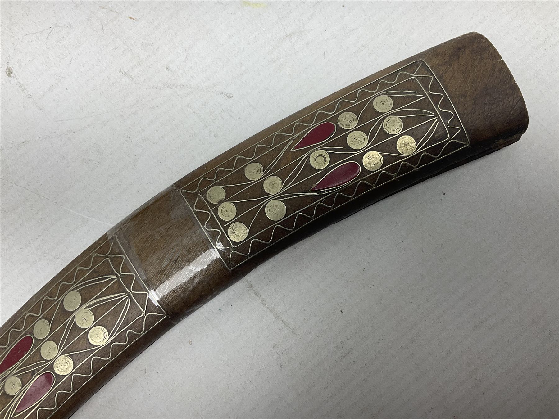 Late 19th/early 20th century Moroccan nimcha dagger-sword, the 40cm curving steel blade with engraved decoration on both sides; shaped hardwood hilt inlaid with brass, white metal wires and red coloured panels; in similarly inlaid scabbard L61cm overall