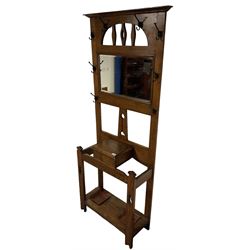 Arts & Crafts period oak hall stand, projecting moulded cornice over arched cut-out decorated with shaped vertical rails, fitted with rectangular bevelled mirror back over hinged glove compartment, on straight pierced supports with shaped pediments 
